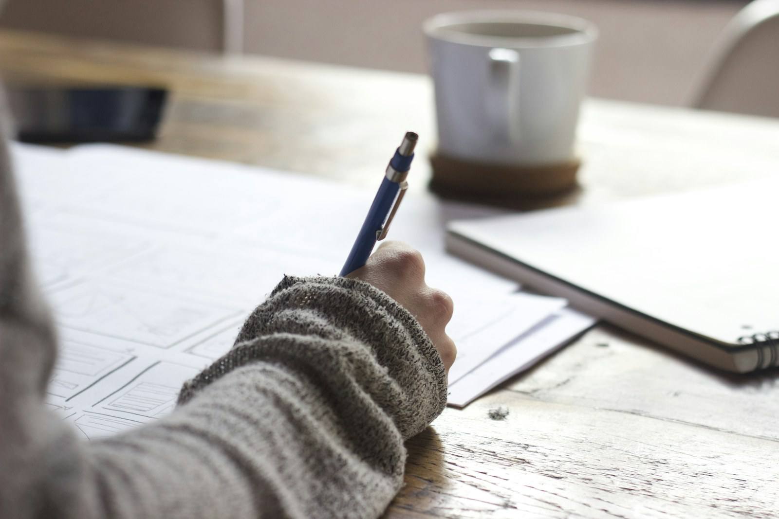 A person writing notes in a notebook at a wooden desk