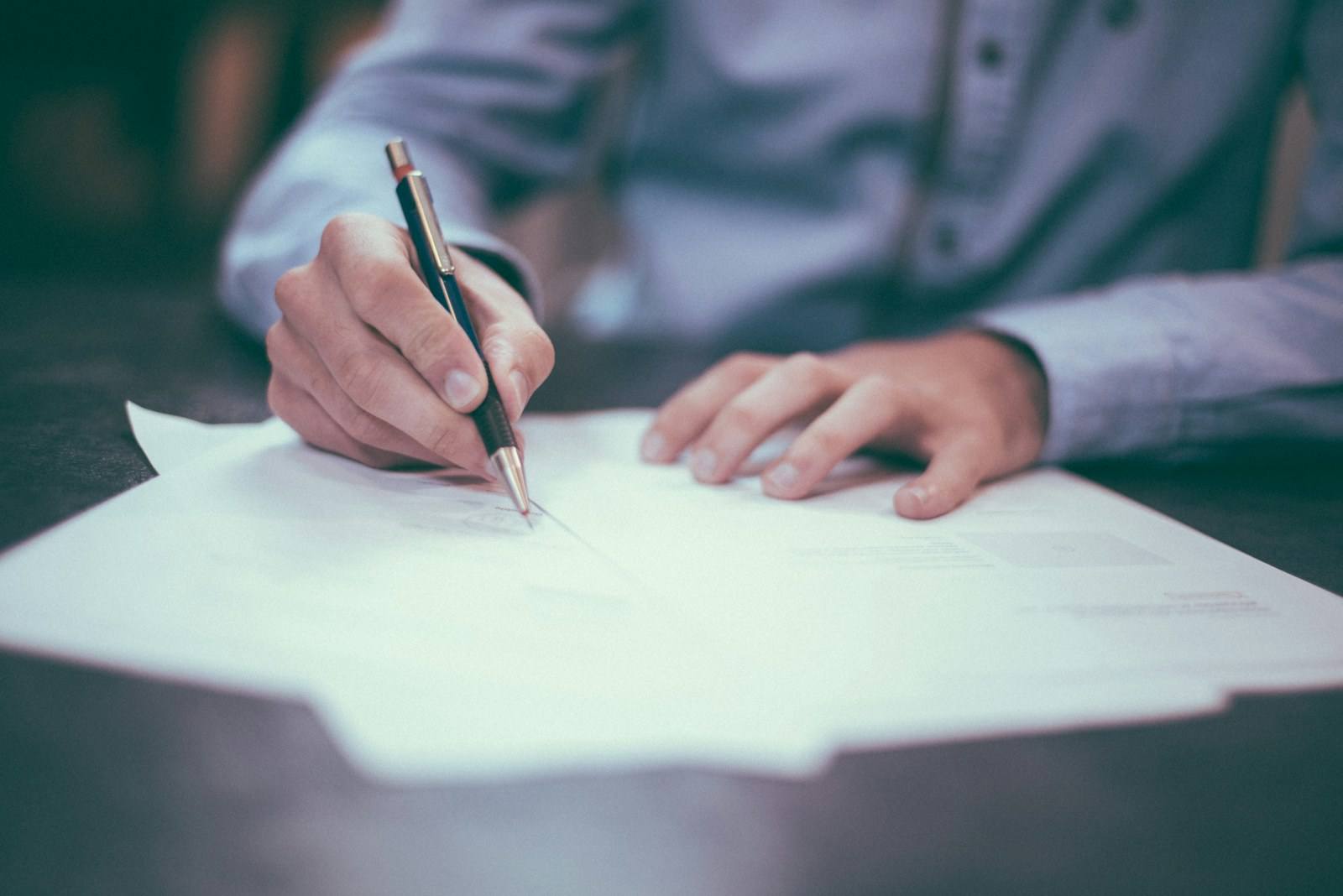 A person signing a document with a pen at a desk